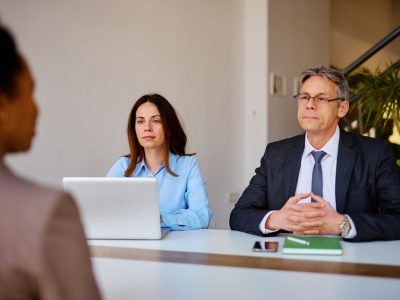 Two human resources managers, a man and a woman, are sitting at a desk in a bright and modern office, interviewing a candidate for a job position, listening carefully to her presentation