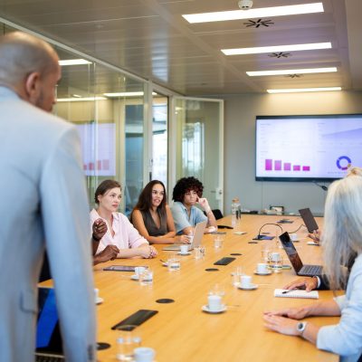 Corporate professional presenting to a diverse group of colleagues during a business meeting in contemporary office